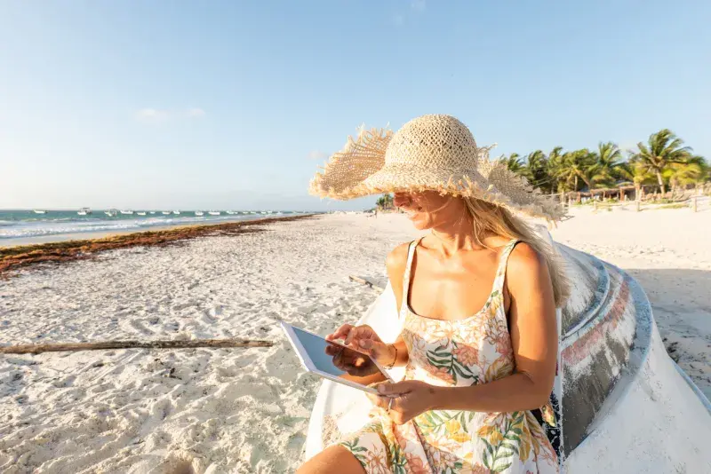 Viajera usando tablet en playa de la Riviera Maya con eSIM activa para México al atardecer