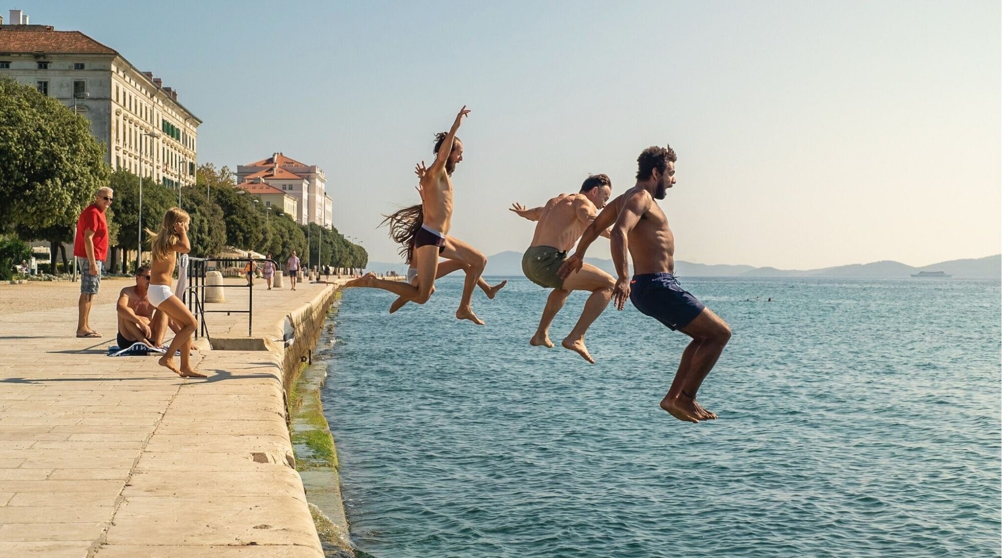 Grupo saltando al mar desde un muelle, viaje con amigos en la costa.