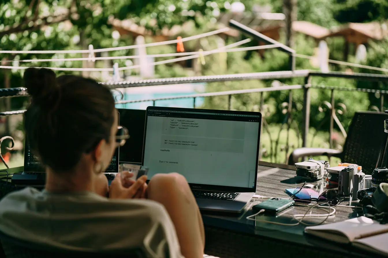 Imagen de una persona de espaldas trabajando en su portátil en una terraza para ilustrar el teletrabajo para los nómadas digitales.