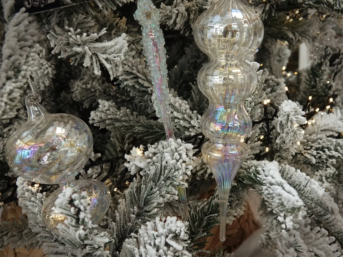 雪で白く色づくクリスマスツリーに飾られているガラス製のオーナメント