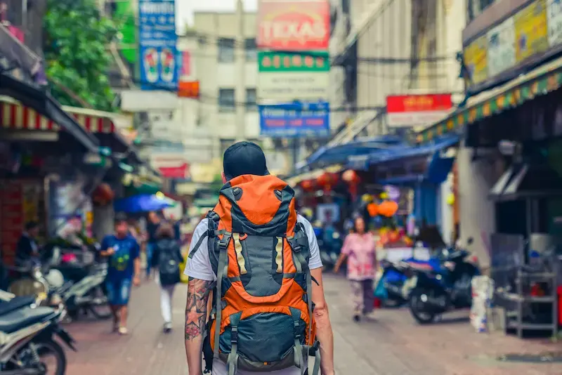 A traveler carrying a large backpack through a street in Bangkok.