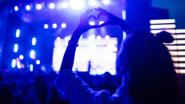 A crowd of excited festivalgoers watching music on a main stage, with a woman in the foreground holding her hands up in a heart symbol, to illustrate the kind of experience you may have at one of the indoor stages when attending Summer Sonic Festival in Japan.