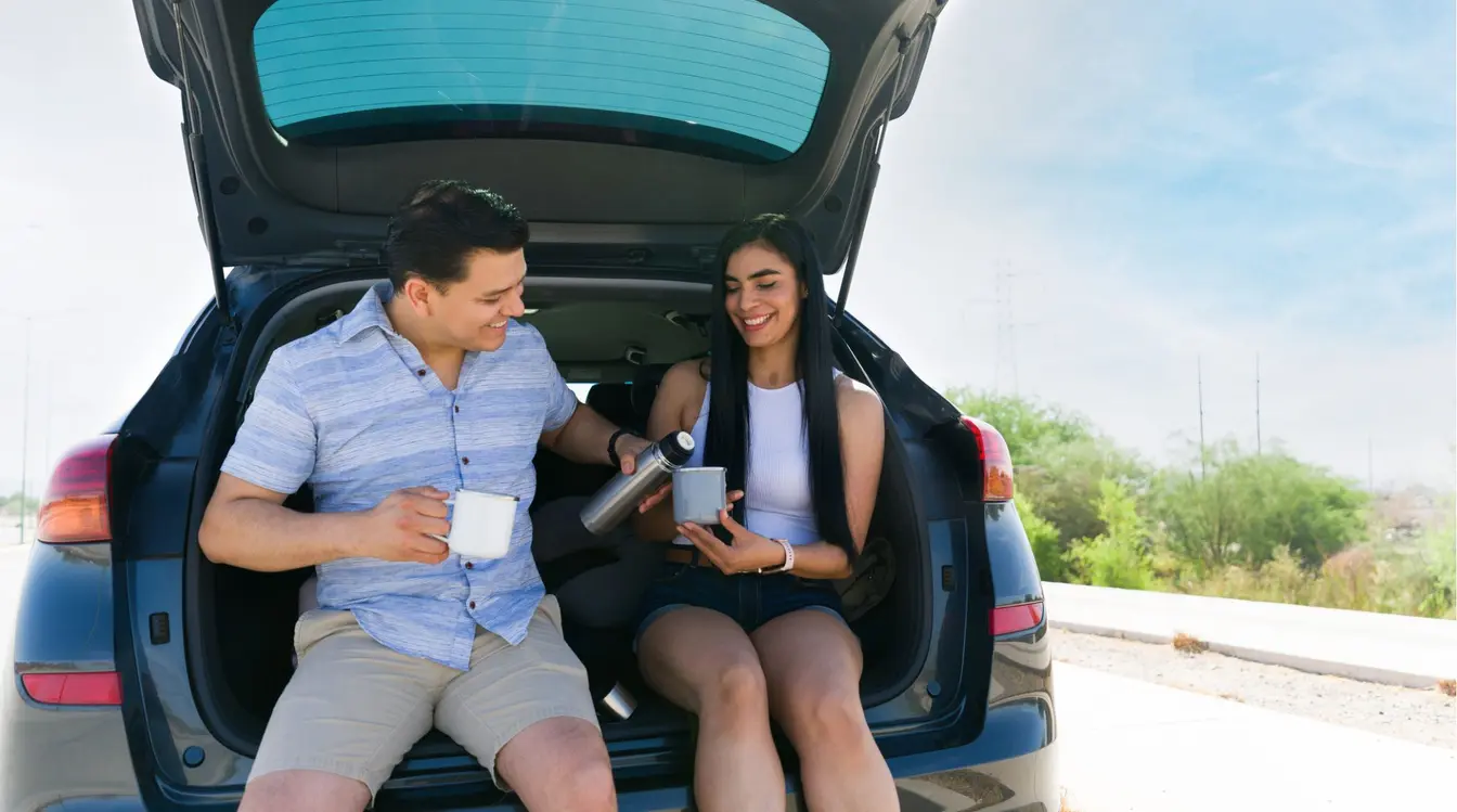 Pareja descansando junto al auto y tomando café durante un viaje por carretera en México.