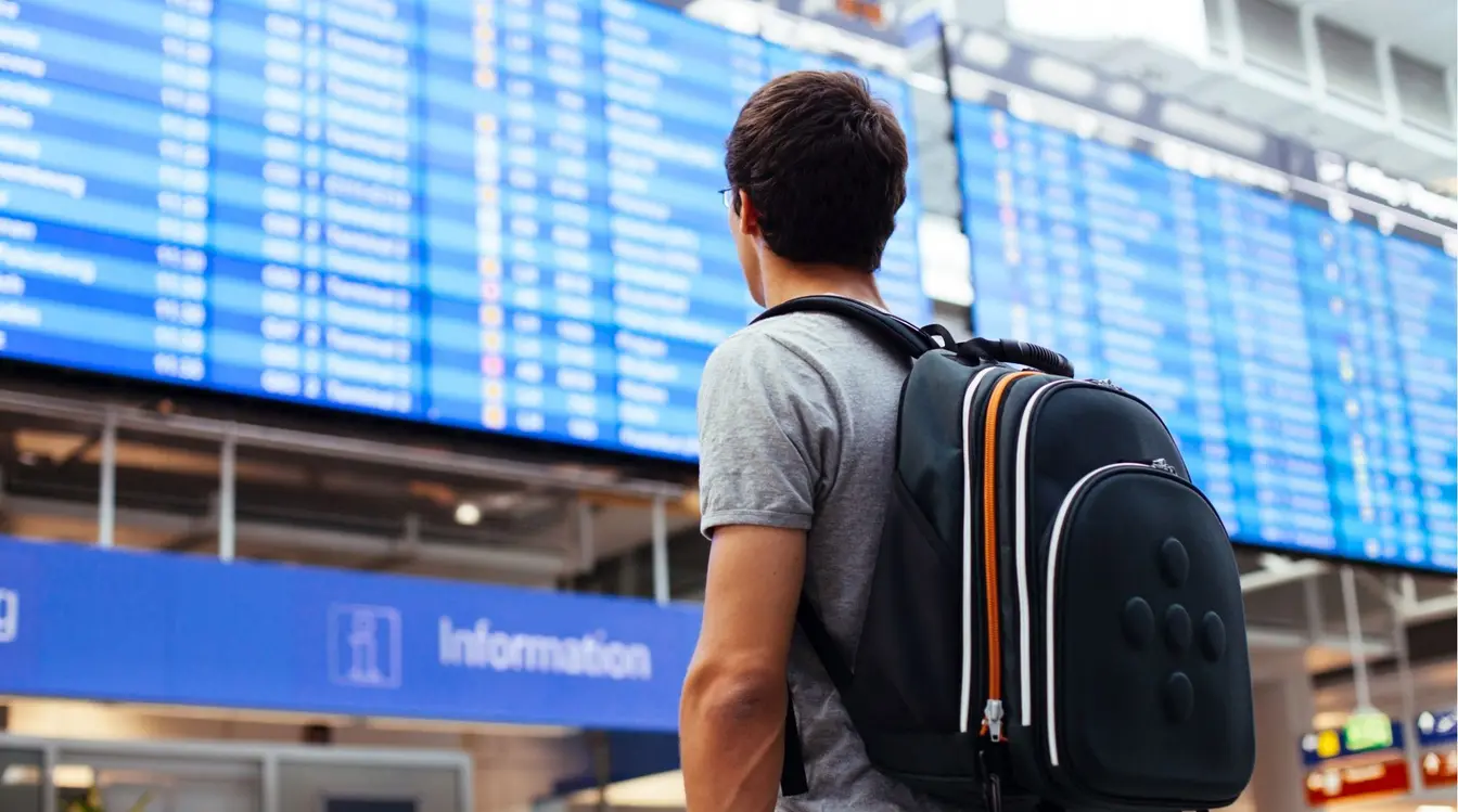 Homme consultant les horaires de départs des avions dans un aéroport, prêt pour un long voyage.