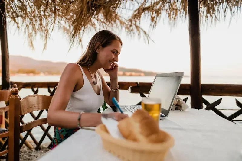 Mujer trabajando de forma remota frente al mar con una laptop y conexión eSIM durante un viaje