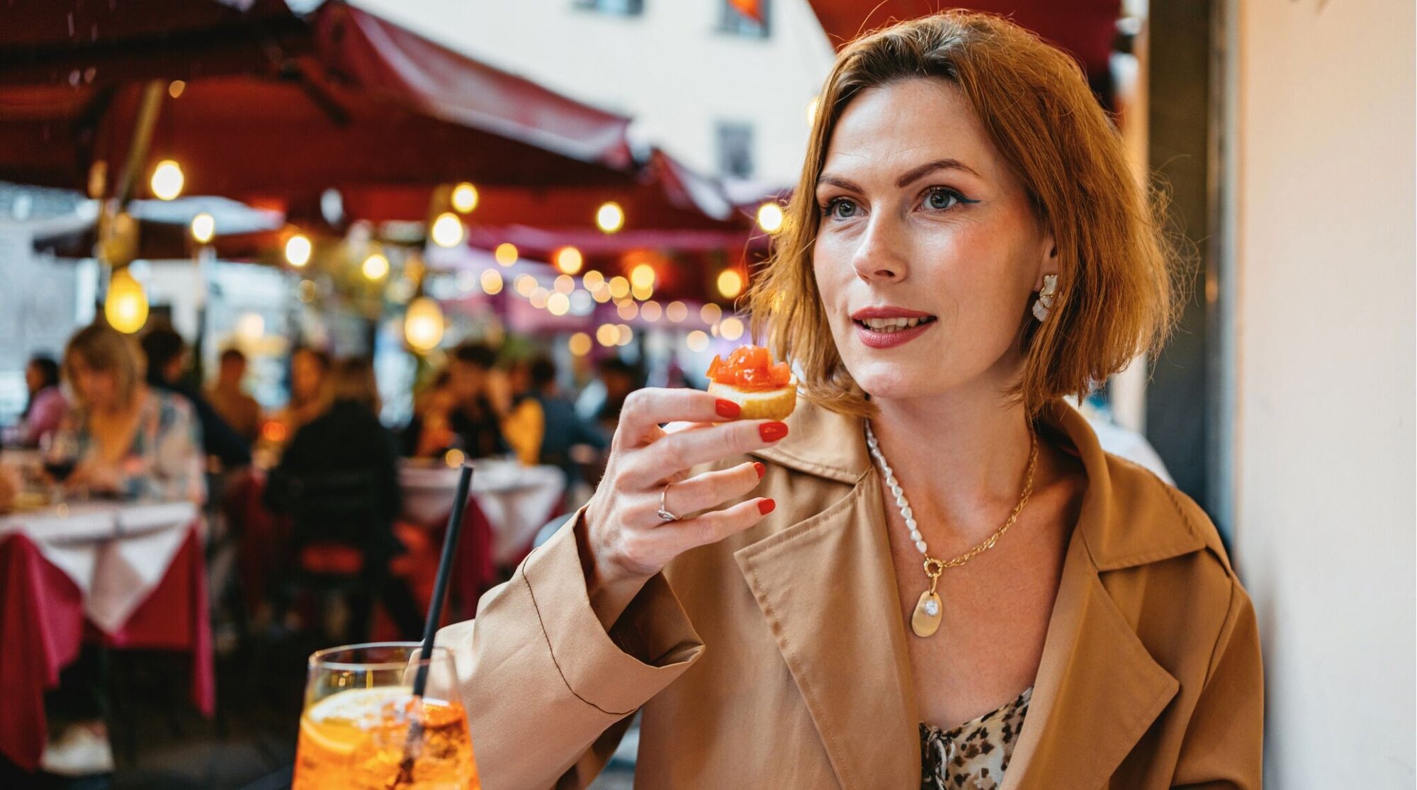 Mulher adulta bebendo coquetel Amaro Spritz e comendo Cicchetti em um café na calçada