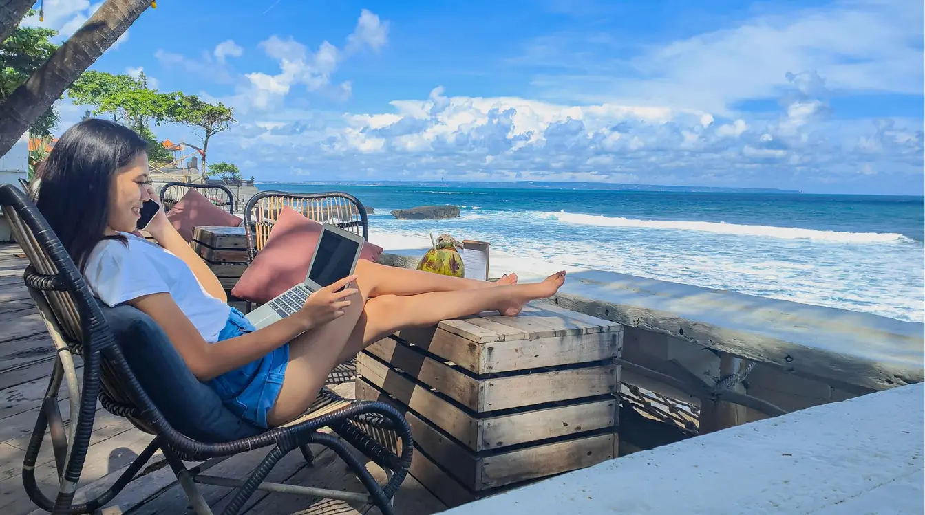 A young woman working on a laptop with a sea view in Bali, hotspotting from an eSIM.