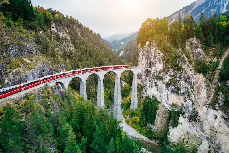 Train rouge traversant le viaduc de Landwasser dans les Alpes suisses, entouré de montagnes et de forêts