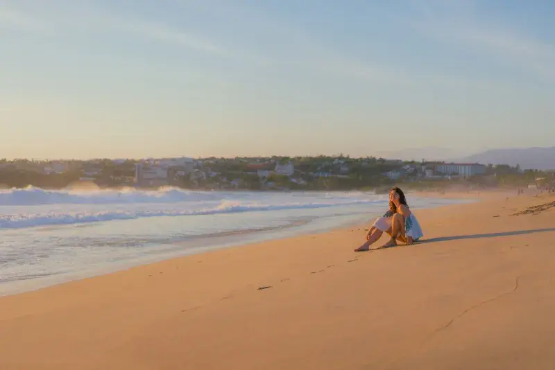 Viajera sentada en la arena mirando el atardecer en Puerto Escondido durante Semana Santa