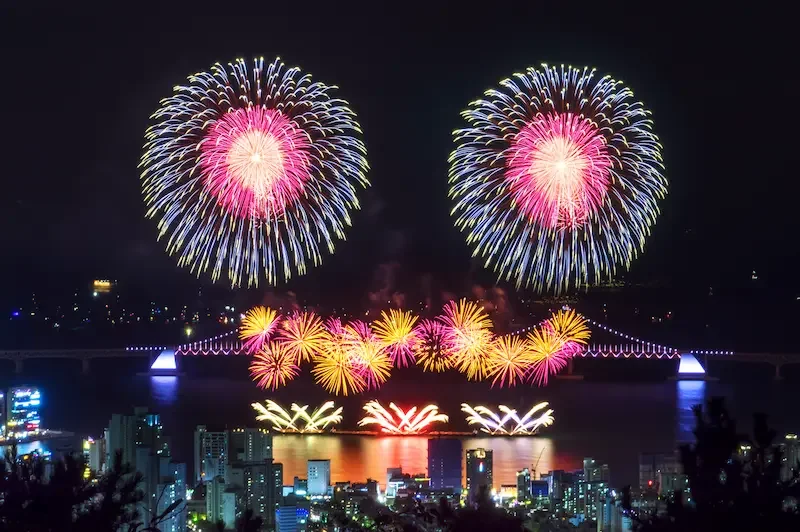 釜山の夜空に大きく打ち上がる「釜山花火祭り」と、ライトアップされた広安里大橋の夜景