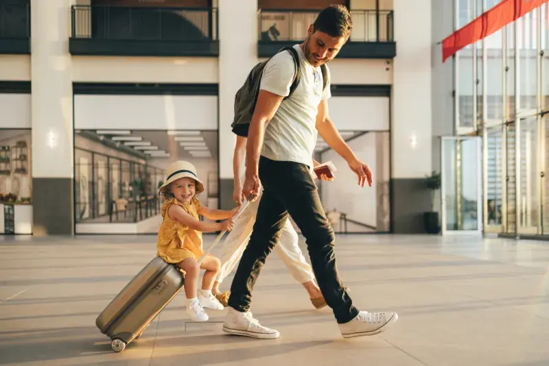 Padre con mochila y maleta caminando en un aeropuerto moderno, listo para instalar su eSIM regional antes de viajar.