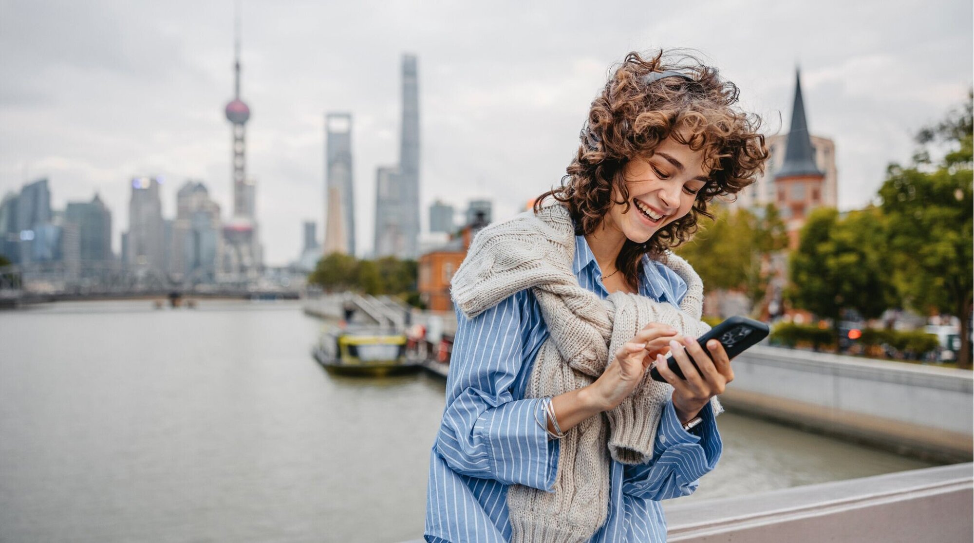 eSIM China: Jovem sorridente usando celular em uma ponte em uma cidade chinesa.