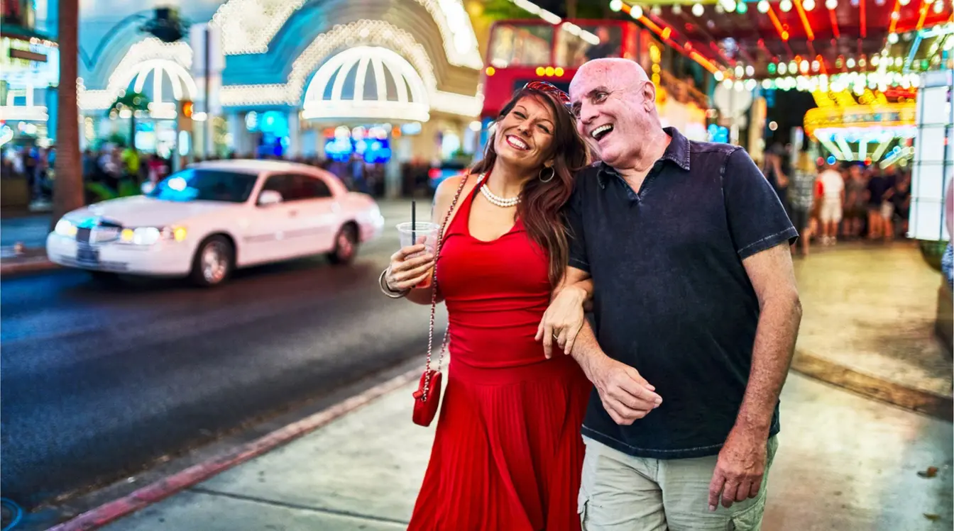 Pareja sonriendo en una calle nocturna de Downtown Las Vegas, con luces y letreros brillantes al fondo.