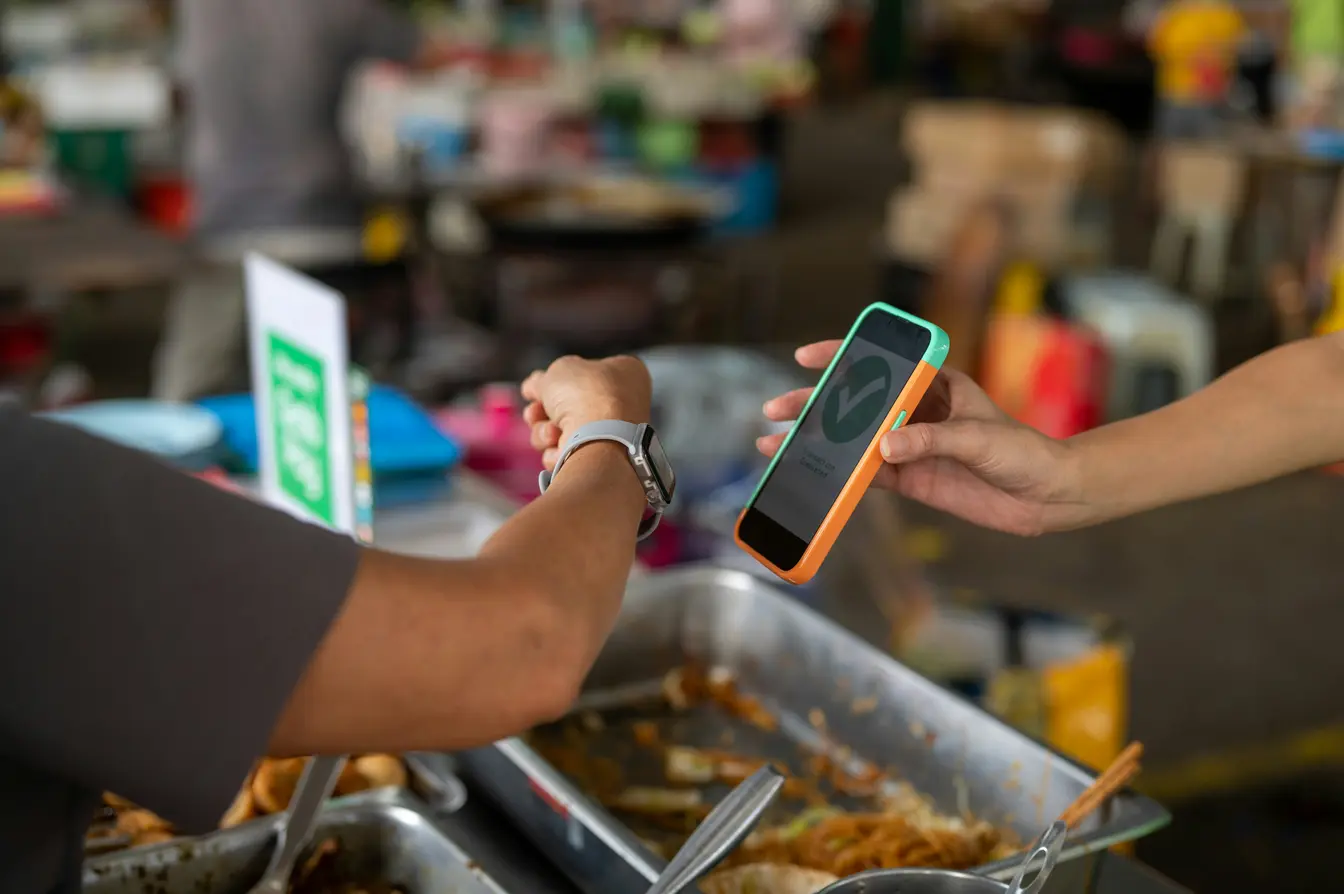 Una persona pagando en un puesto de comida callejera con un reloj inteligente usando datos móviles.
