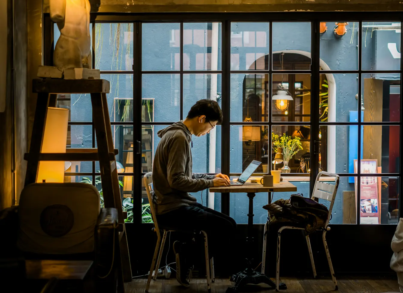 Imagen de una persona sentada en una cafetería delante de su portátil para reflejar el teletrabajo.