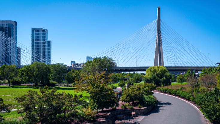 Paul Revere park in Boston, filled with green trees and with the Zakim bridge and tall buildings in the background.