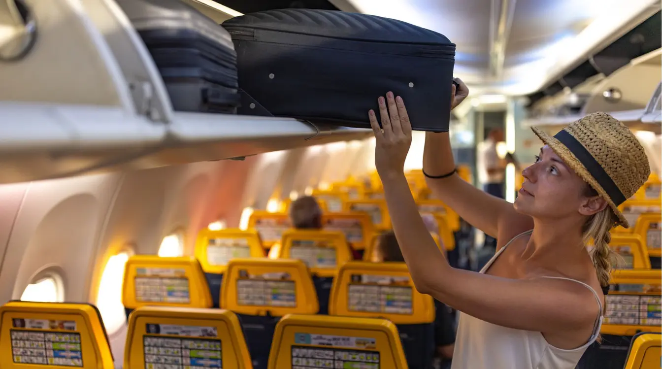 Uma turista coloca a mala no compartimento superior do avião em um voo low cost.