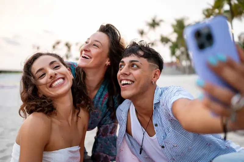 Grupo de amigos tomándose una selfie en la playa con un smartphone durante un viaje.