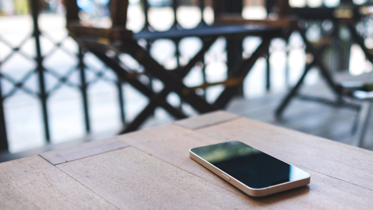 A photograph of an iPhone alone on the outdoor table of a cafe or restaurant after someone has lost it of left it there accidentally, to illustrate a blog post entitled 'Is my iPhone eSIM-compatible?'