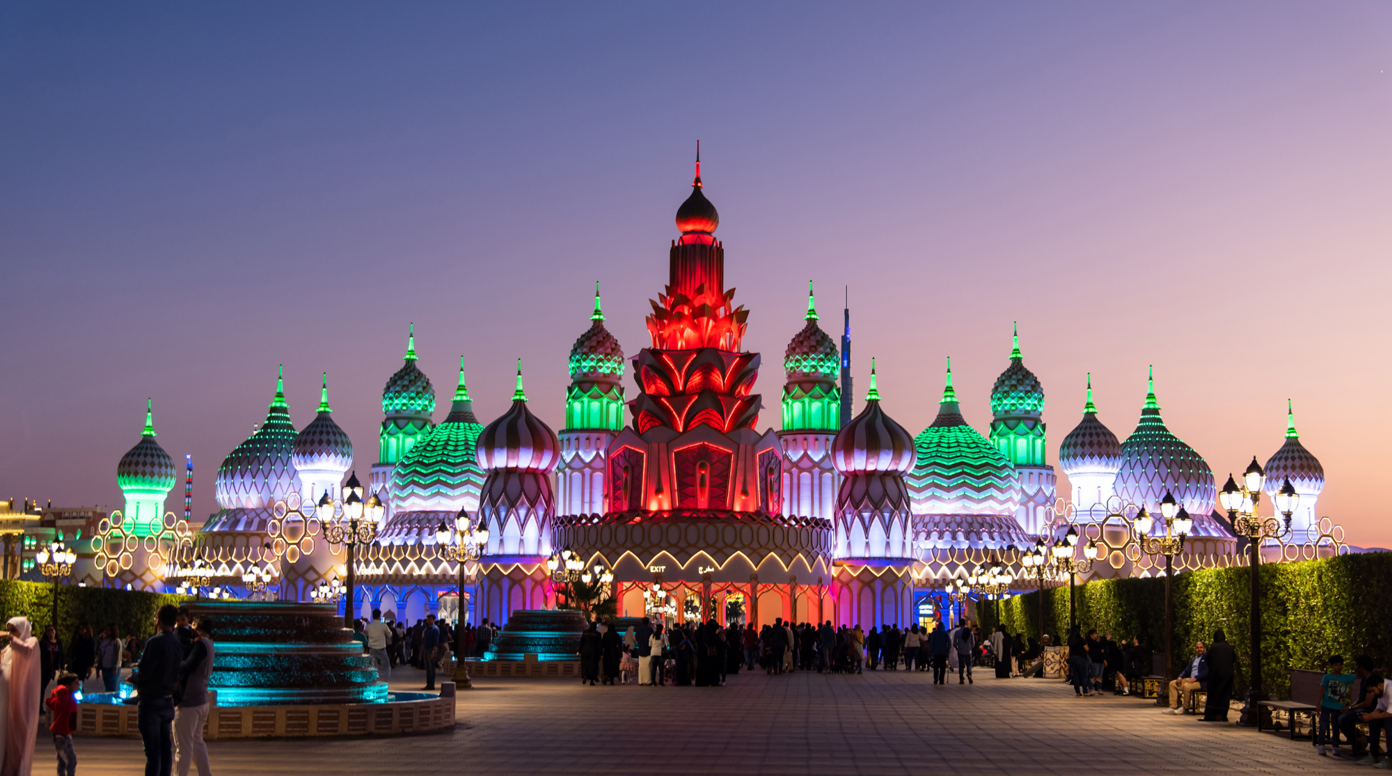 إضاءة مذهلة لبوابة القرية العالمية دبي عند الغروب مع حشود الزوار وألوان مبهرة تعكس أجواء الموسم في 2025