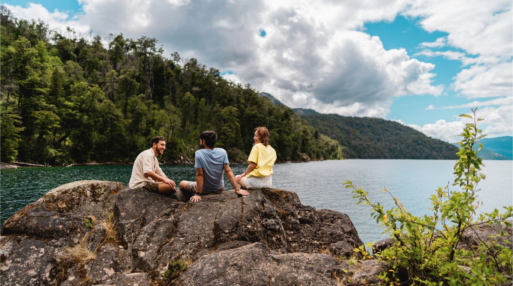 Un grupo de amigos conversando en la cima de una montaña con vistas a un lago en la Patagonia.