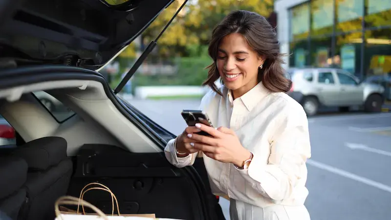 Mujer revisando su celular junto al auto después de cruzar a Estados Unidos, tras una jornada de compras.