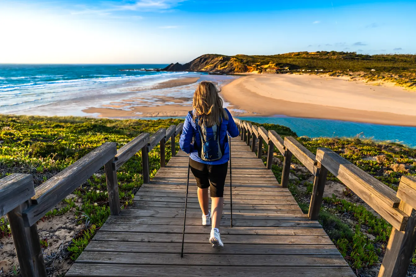 Donna che pratica nordic walking su passerella in legno vicino alla spiaggia Amoreira Praia in una giornata primaverile di maggio.