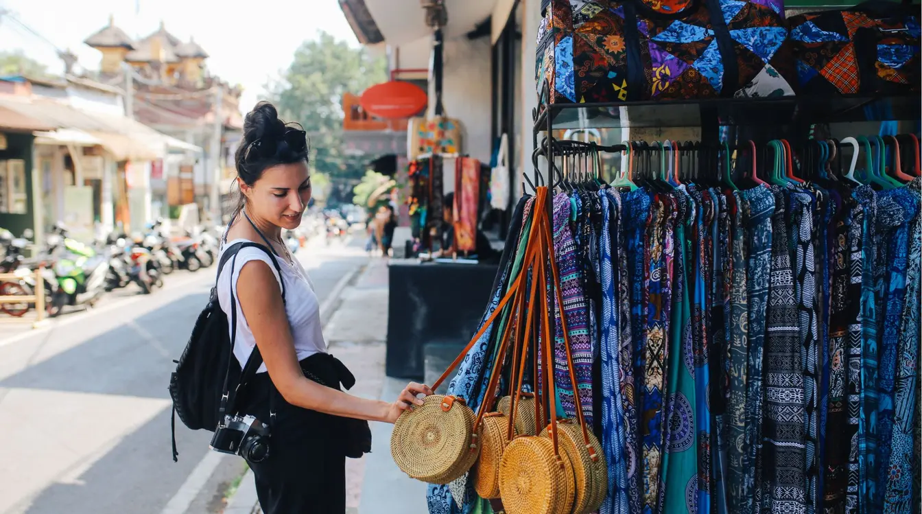 A woman browsing bags and colorful trousers at a street stall in Ubud, Bali.