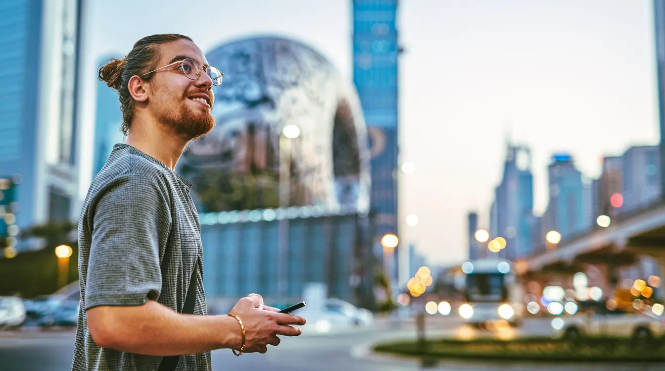 A man in a blue coat holding a yellow phone smiles after finding the best international roaming plans UK eSIMs offer. 
