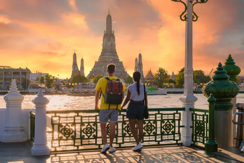Pareja con mochilas mirando un templo iluminado al atardecer desde un mirador.