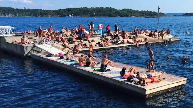 Norwegians enjoying outdoor life by relaxing on a floating wooden dock in a calm blue fjord during summer. 