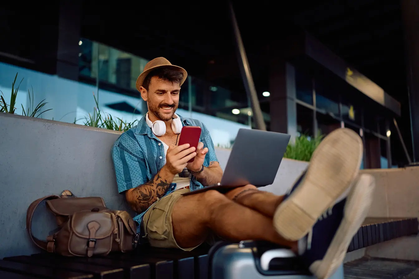 Una persona mirando su teléfono celular mientras usa una computadora portátil en el aeropuerto. 