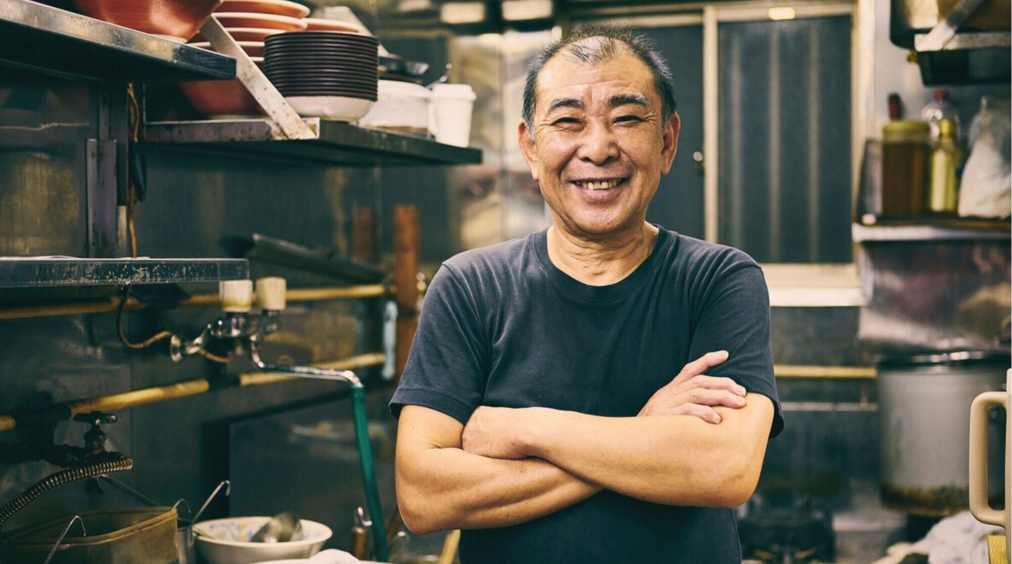 Dueño de una tienda de ramen japonesa sonriendo detrás de la barra del restaurante.