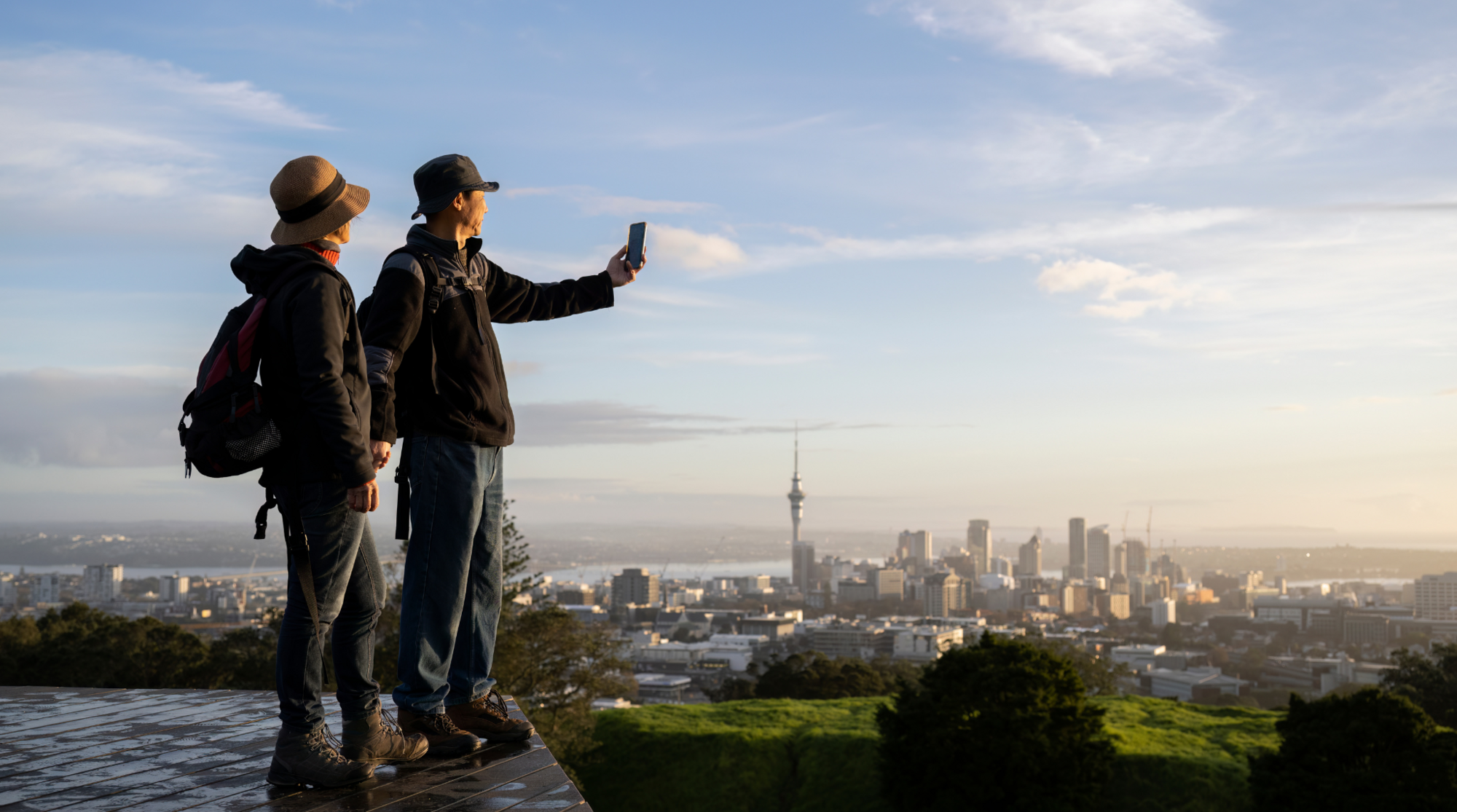 Ein Paar steht auf einem Hügel vor Auckland in Neuseeland und benutzt ihre SIM-Karte, um ein Foto zu schießen