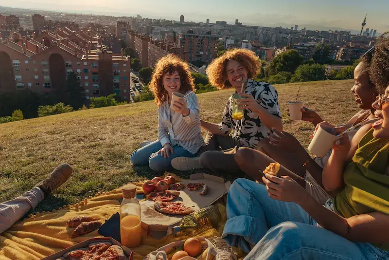 Grupo de amigos haciendo un picnic con vista a la ciudad de Madrid al atardecer.