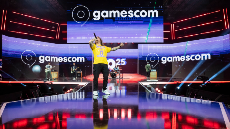 A man in a yellow t-shirt shouts excitedly into a microphone on the stage of gamescom Germany in 2025.