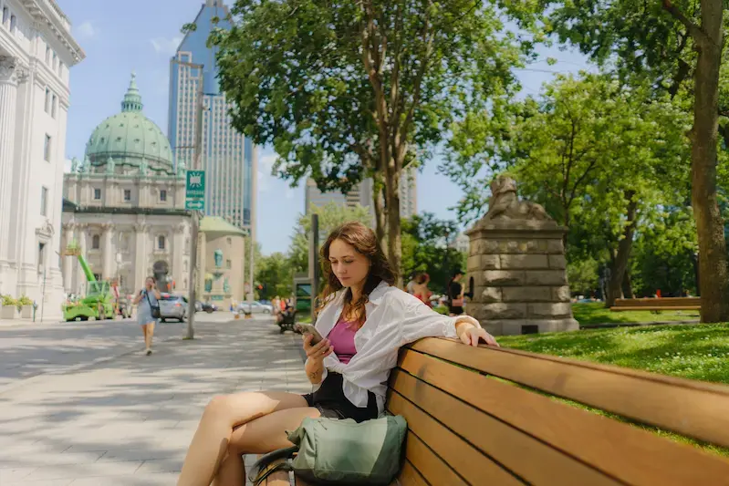 Mujer usando su celular en una banca de Montreal durante un viaje a Canadá 