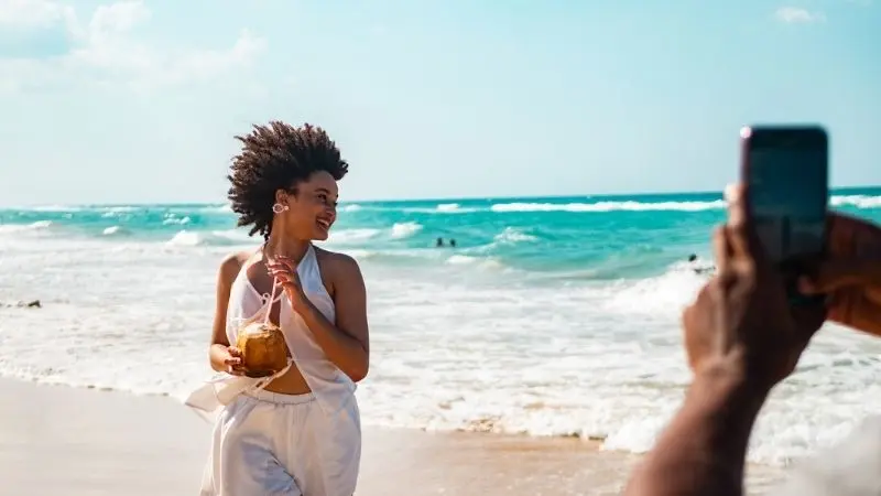 Eine Frau mit Kokosnuss in der Hand posiert für ein Foto an einem Strand in der Karibik 