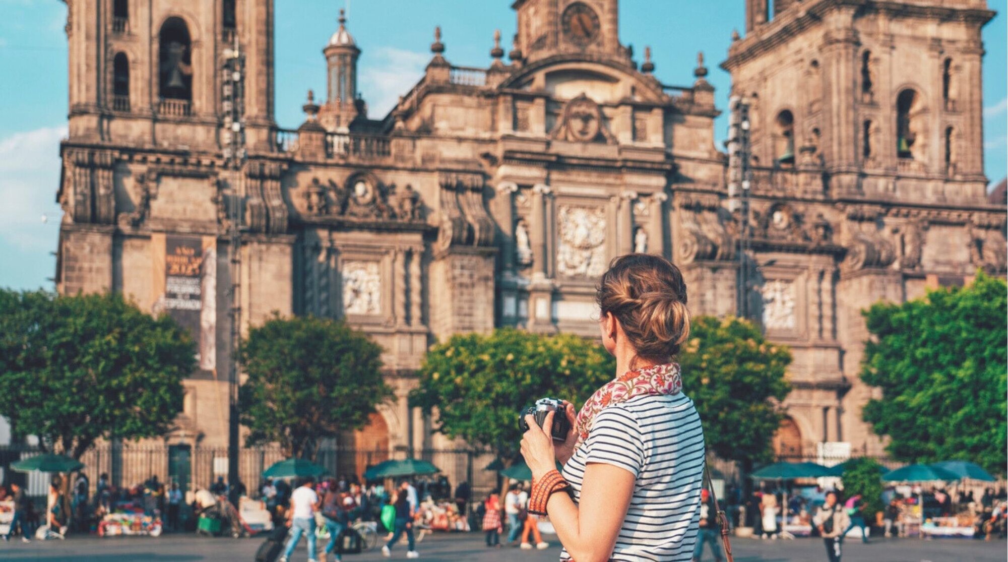 Mujer tomando fotos frente a una catedral en una gran plaza, ambiente turístico y cielo despejado.