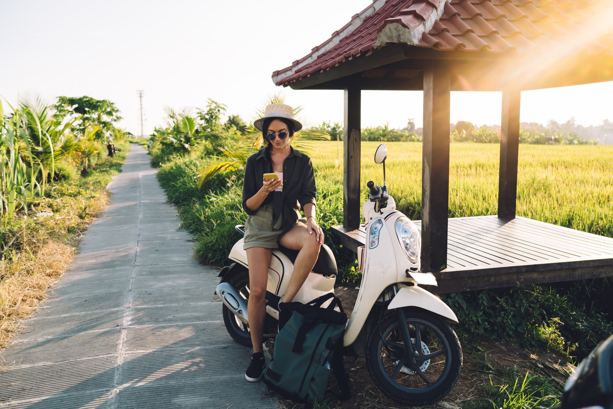 Jeune femme voyageuse appuyée sur son scooter en zone rurale à Bali, regardant son smartphone connecté via une eSIM avec Airalo.