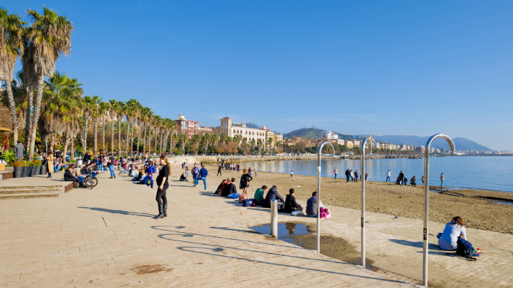 A colour photo of Santa Teresa, the urban beach in Salerno, showing locals sitting on the sand by the bright blue sea.