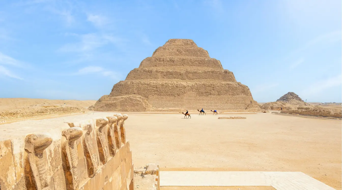 Hommes à dos de dromadaire devant la pyramide à degrés de Djéser, sur le site archéologique de Saqqarah en Égypte.