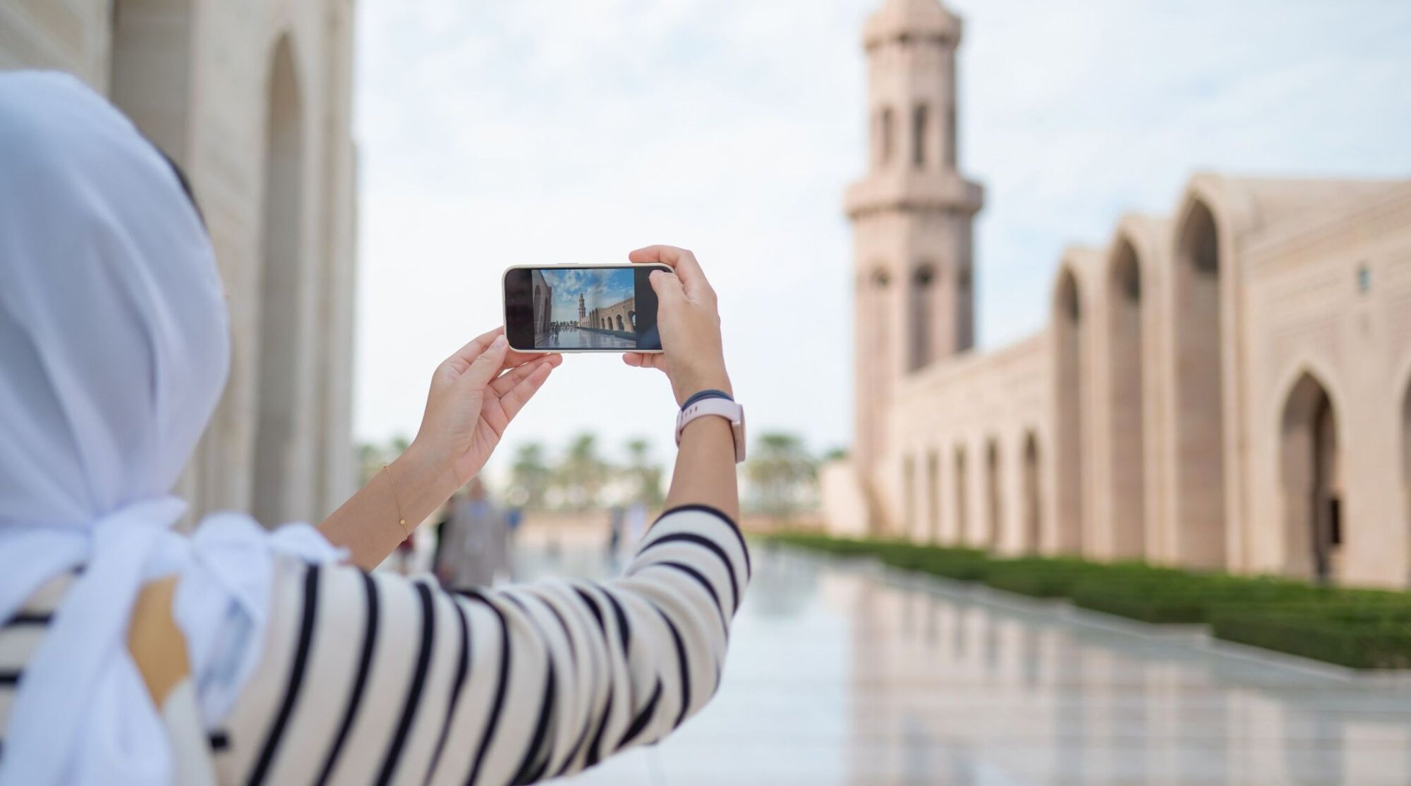 Donna che fotografa la Grande Moschea del Sultano Qaboos a Muscat, in Oman, utilizzando lo smartphone durante il viaggio.
