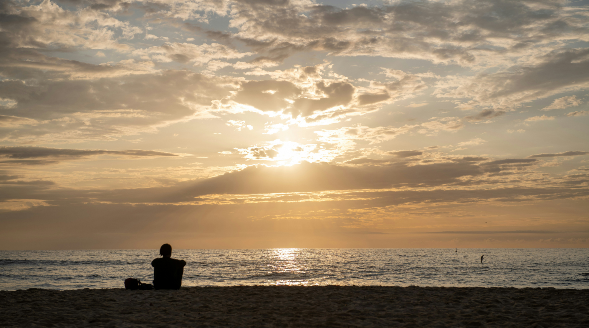Person sitzt während des Sonnenuntergangs am Strand