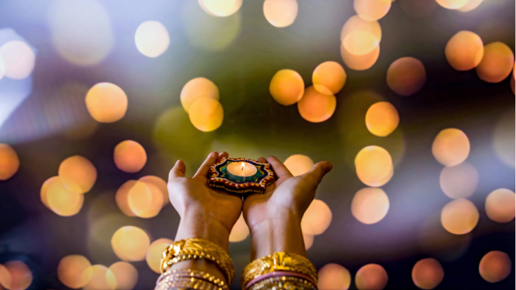 An Indian woman's hands decorated with henna patterns as she holds a lit candle.