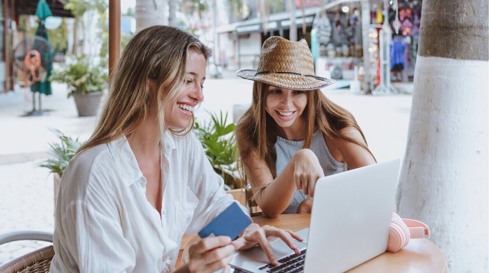 Jovens amigas latinas usando laptop para fazer compras com cartão de crédito na praia no México