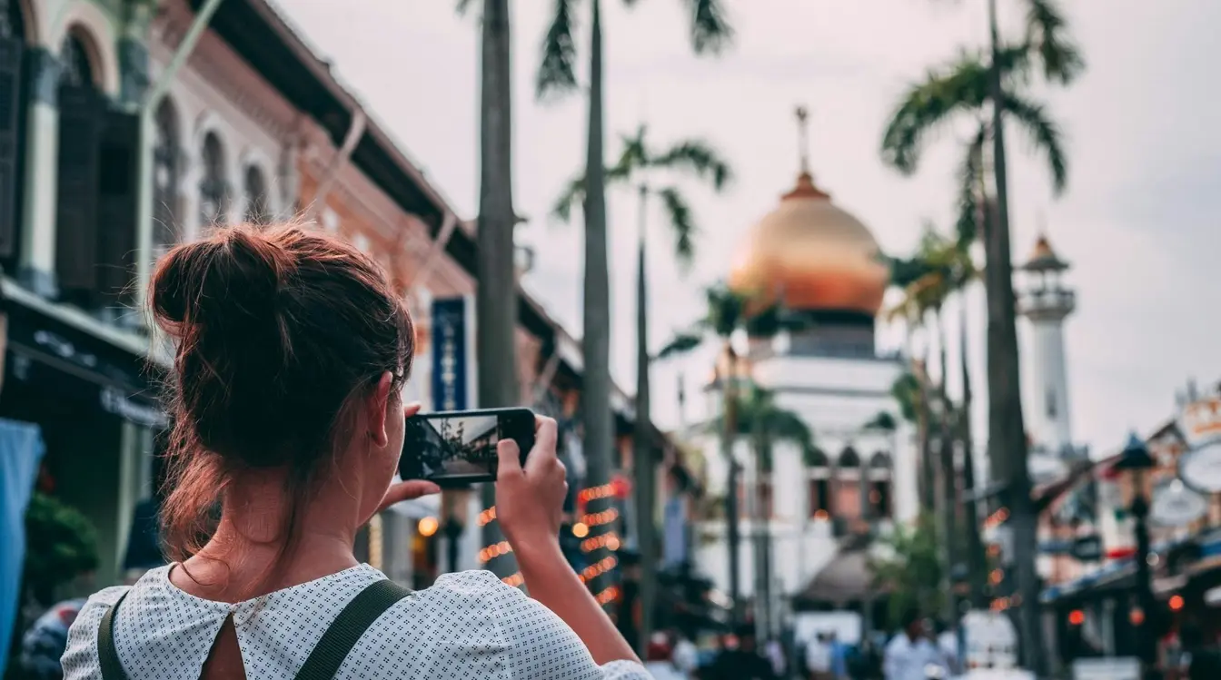 A woman using her phone to photograph the Sultan Mosque from a street in Singapore.