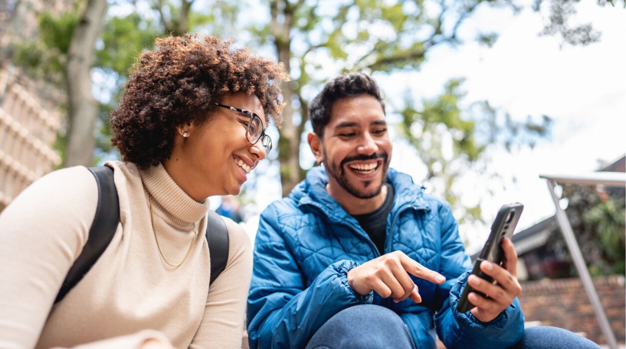 Jovem mostrando algo no celular para amiga em uma escada ao ar livre.
