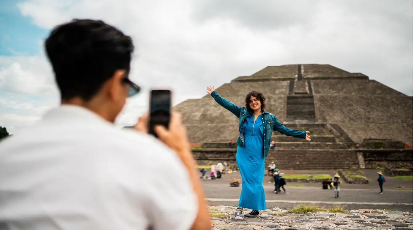 Turista posando frente a una pirámide en Teotihuacán mientras otra persona toma una foto
