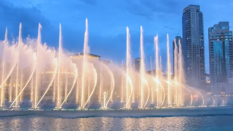 Spouts of water illuminated by warm lights shoot up into the air in front of Dubai's skyscrapers.